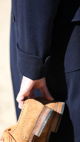 Cyril sur la plage de Trouville tient la paire de Richelieu Weston en veau velours couleur noisette, et porte le manteau polo-coat Bart en laine et cachemire coloris bleu nuit de la collection Automne-Hiver 2024 de la  Maison Gabriel Paris - Détail du manteau et de la manche officier