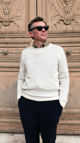 Cyril pose devant une porte du musée du Louvre et porte le pull Aimé en baby cachemire blanc cassé de la Maison Gabriel Paris