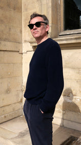 Cyril pose dans la cour du musée du Louvre et porte le pull Jean-Paul en côtes anglaises col rond coloris bleu marine de la Maison Gabriel Paris
