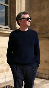 Cyril pose dans la cour du musée du Louvre et porte le pull Jean-Paul en côtes anglaises col rond coloris bleu marine de la Maison Gabriel Paris