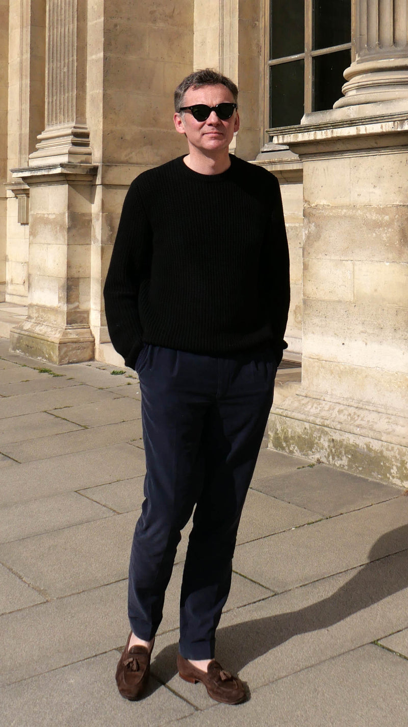 Cyril pose dans la cour du musée du Louvre et porte le pull Jean-Paul en côtes anglaises col rond coloris noir de la Maison Gabriel Paris