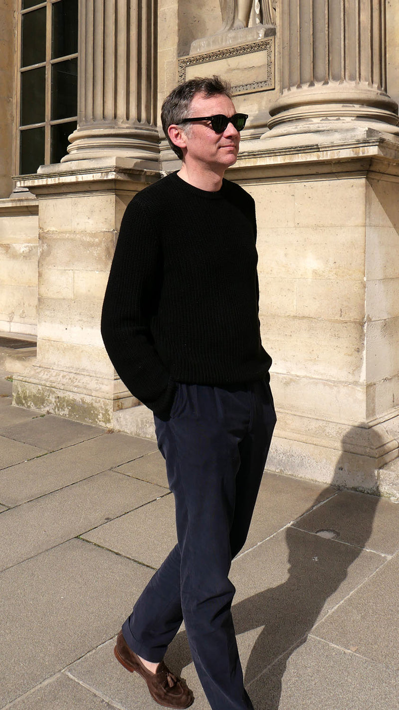 Cyril pose dans la cour du musée du Louvre et porte le pull Jean-Paul en côtes anglaises col rond coloris noir de la Maison Gabriel Paris